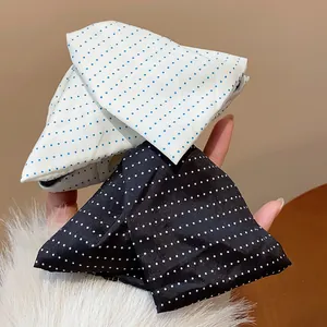 Vue détaillée de pinces à cheveux élégantes en tissu à pois noirs et blancs en main.