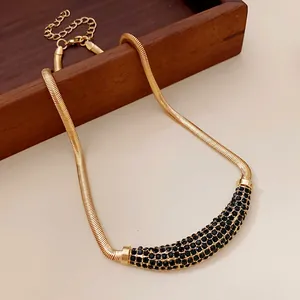 Close-up of gold snake chain necklace with black rhinestone crescent pendant