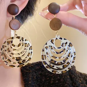 Close-up of leopard print acrylic drop earrings with dark wood studs and hollow circle design.