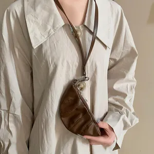 Vista detallada del collar monedero de croissant de cuero sintético marrón en camisa.