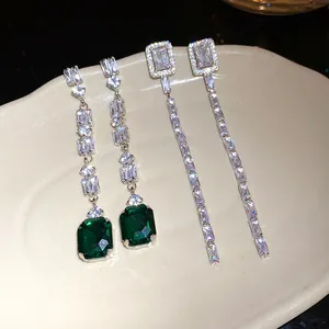 Close-up of elegant emerald and clear zircon square tassel earrings on a ceramic plate