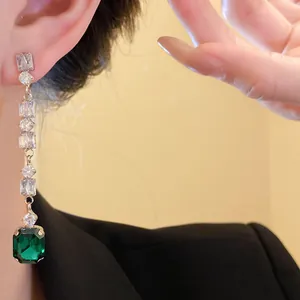 Detail of elegant silver needle dangling earrings with emerald cut green zircon stone