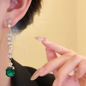 Detailed close-up of luxurious emerald green square gemstone earrings with sparkling white zircons