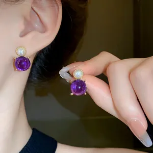 Detailed shot of elegant gold-tone earrings featuring purple round stones and pearls