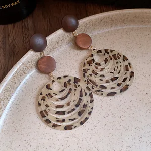 Close-up view of leopard print hoop earrings with wooden studs on a ceramic plate