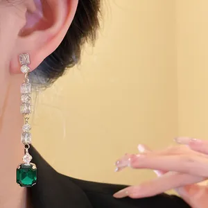 Close-up detail of elegant long tassel earring featuring a large emerald green stone and zircons.