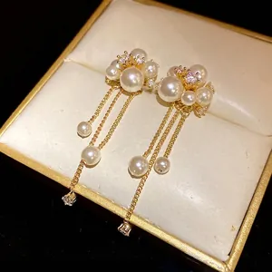 Elegant flower stud earrings with pearls, zircons, and long gold tassels in jewelry box.
