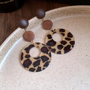 Close-up of leopard print and wooden disk drop earrings on a speckled ceramic plate