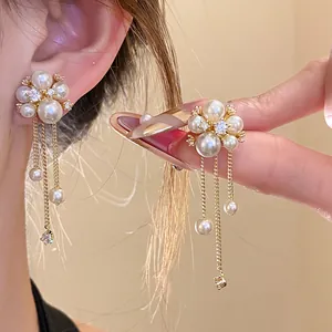 Close-up of elegant pearl flower earrings with zircon tassels and gold-plated chains.
