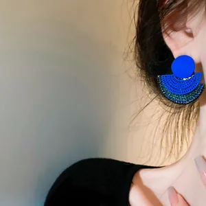 Detailed close-up of vibrant blue fan-shaped engraved metal earrings on model.