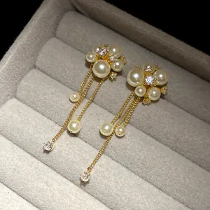 Close-up of elegant gold flower earrings with pearl tassels and sparkling zircons
