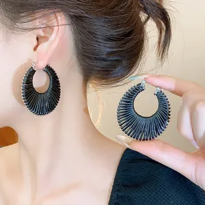 Close-up detail of stylish black woven circular hoop earrings with a textured surface.