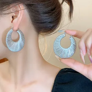 Close-up of silver textured hoop earrings showing intricate woven-style pattern details
