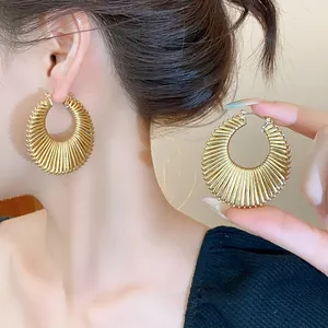Close-up of golden textured hoop earrings showing intricate hollowed-out design details
