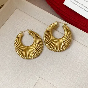 Detailed close-up view of elegant gold textured hollow hoop earrings on a beige fabric