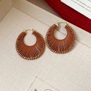Macro view showing detail of brown woven leather hoop earrings with gold-toned metal hooks