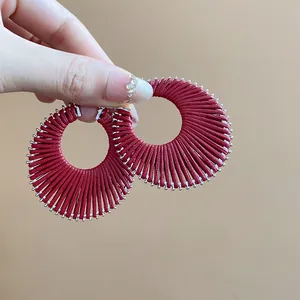 Close-up of circular hoop earrings wrapped in dark red thread with silver accents