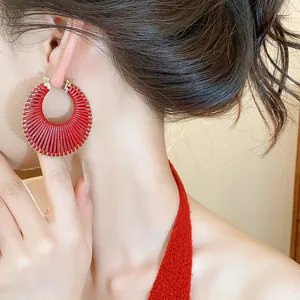 Close-up of red woven hoop earring on model, showcasing detailed texture and design.