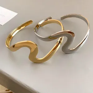 Close-up of wavy metal open bangles in gold and silver with minimalist twisted design.