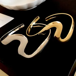 Detailed view of elegant gold and silver wavy metal open bracelets on black velvet