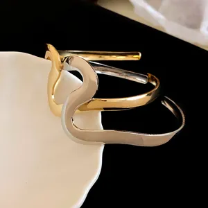 Close-up view of minimalist wavy metal open bangles in polished gold and silver finishes