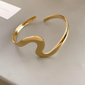 Detail showing the polished finish and unique wavy design of a gold open cuff bracelet