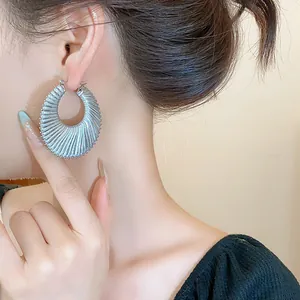 Detailed view of large silver-toned textured hollow hoop earrings on an elegant model