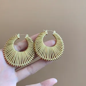 Detailed close-up view of golden round hollow sunburst earrings held against a tan background