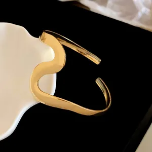Close-up of golden wave-shaped metal open bangle with minimalist distorted design