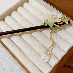 Detailed macro view of a white flower wooden hairpin with gold tassel in a display box.