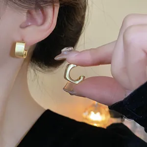 Primer plano de pendientes en forma de C de oro cepillado en la oreja y en la mano