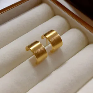 Primer plano de pendientes geométricos cepillados oro en un joyero de terciopelo blanco
