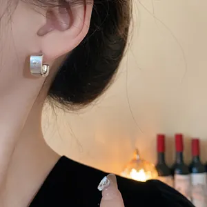 Detalle de un pendiente de aro cuadrado de plata cepillada minimalista en el lóbulo de la oreja