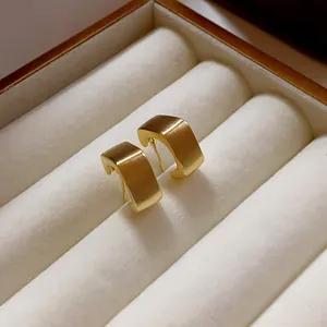 Vista de detalle de los pendientes geométricos cuadrados cepillados en oro.