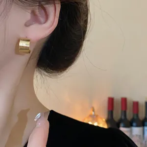 Primer plano de elegantes pendientes de aro anchos dorados cepillados en una modelo