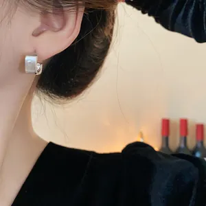 Detalle de pendientes geométricos cuadrados de plata cepillada de estilo minimalista.