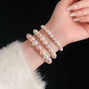 Detailed view of three-layer elastic pearl bracelets in white and pink on wrist.
