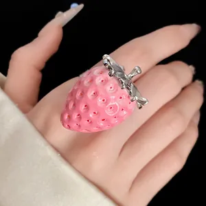 Close-up of a sweet pink resin strawberry ring on a hand with black background