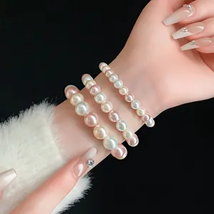 Detailed view of three layered elastic pearl bracelets in cream white and pink on wrist.