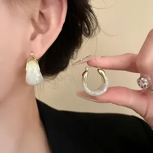 Close-up of white marble pattern U-shaped basket hoop earrings with gold details