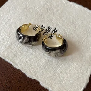 Detail view of U-shaped basket hoop earrings with black marbled resin and gold accents