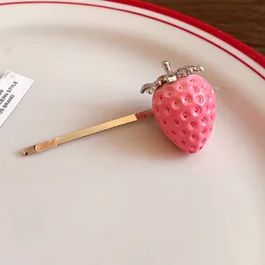 Detail shot of a cute pink resin strawberry hair clip resting on a white ceramic plate.