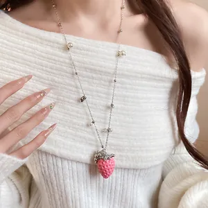 Detailed view of a sweet pink strawberry pendant necklace worn over a white sweater