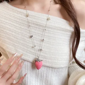Detail view of a cute pink strawberry pendant necklace with white pearls on a model.