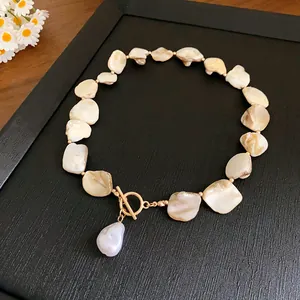 Close-up detail of a handmade shell necklace with baroque pearl and a gold toggle clasp.