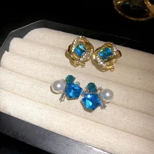 Pendientes elegantes con piedra cuadrada azul y perlas en una bandeja de joyería beige.