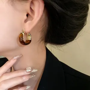 Close-up of retro U-shaped basket earrings with brown marbled resin and gold finish