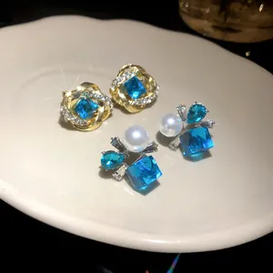 Detalle de primer plano de pendientes con cristal azul y perla sobre un plato blanco