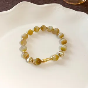 Primo piano di un elegante bracciale di perle con ciondolo a pesce dorato e pietre occhio di gatto.
