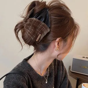 Close-up detail of a vintage plaid and leather bow hair claw clip worn by a model